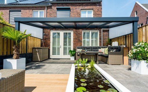 Terrassenüberdachung mit Glasdach und Loungebereich vor einem Backsteinhaus